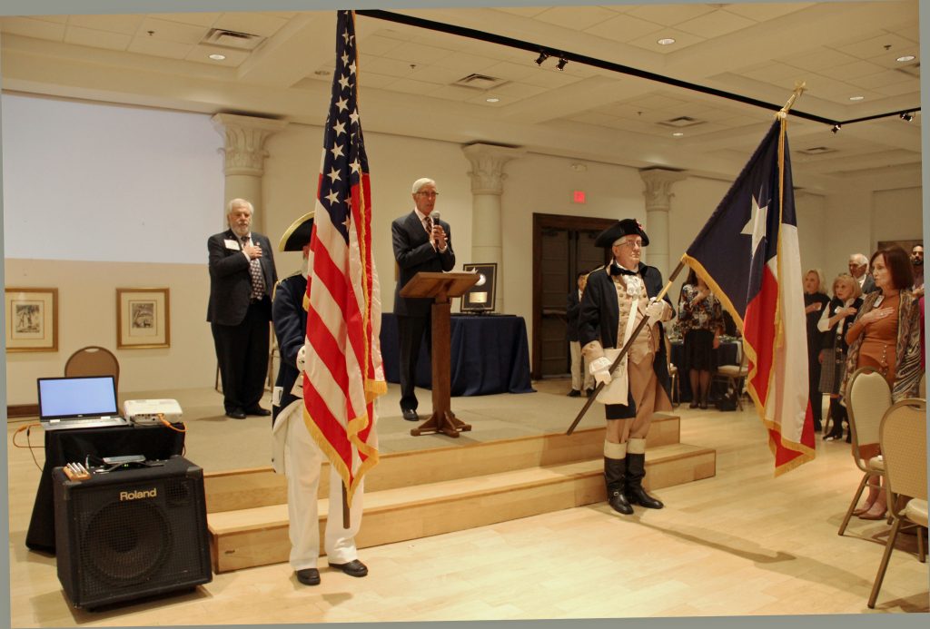 Adult talking into microphone at podium next to flags
