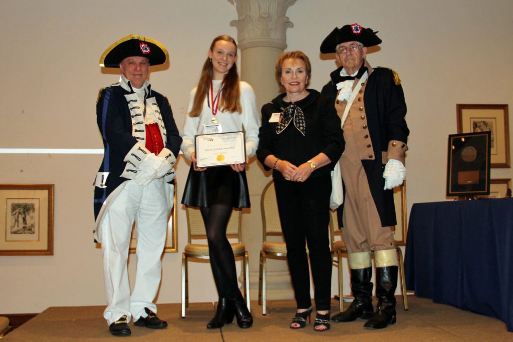 Adult and student with award standing next to two adults in historical costumes
