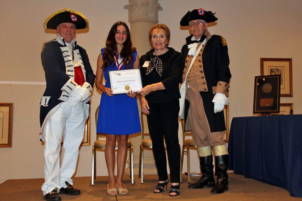 Adult and Student holding award standing next to two adults dressed in historical costumes