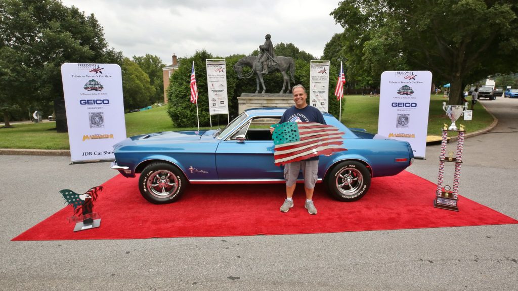 Adult holding American Flag standing in front of vintage car