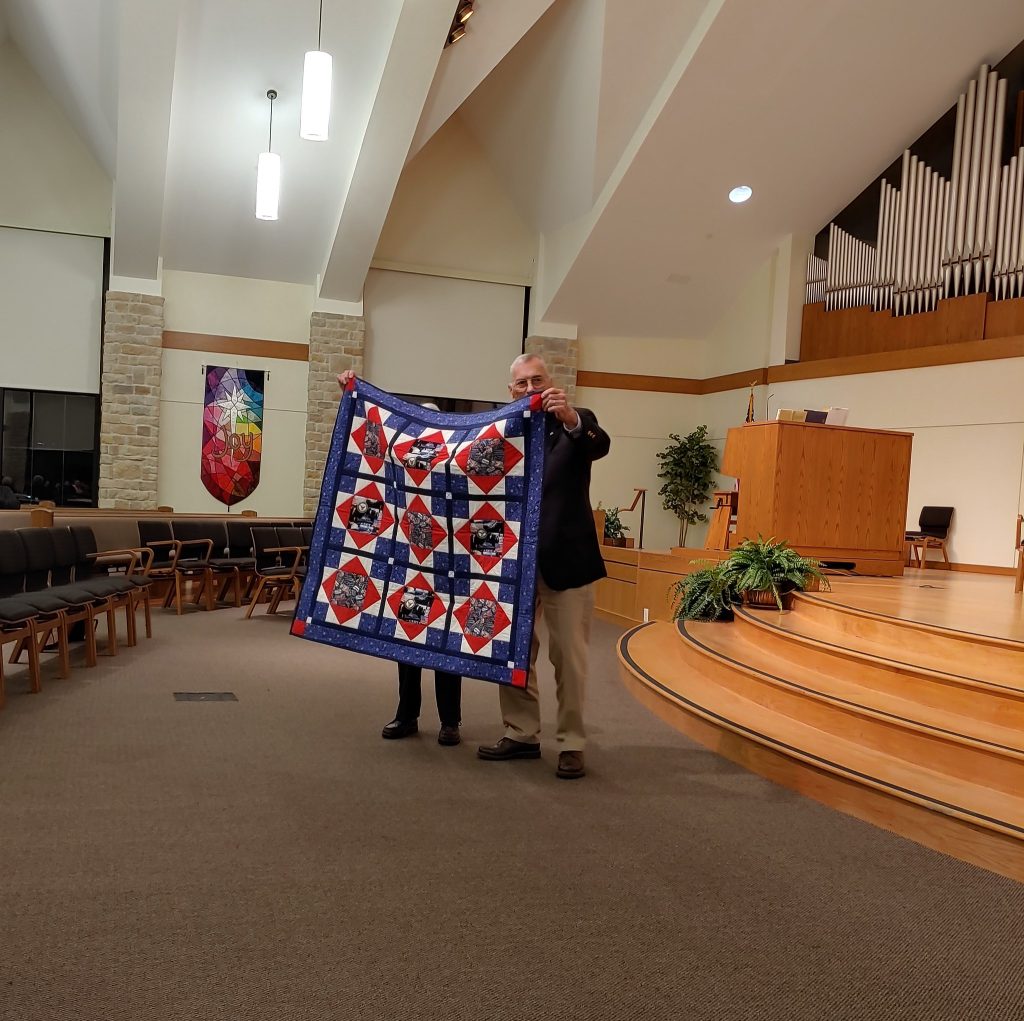 Man holding up a quilt at a Veteran event.