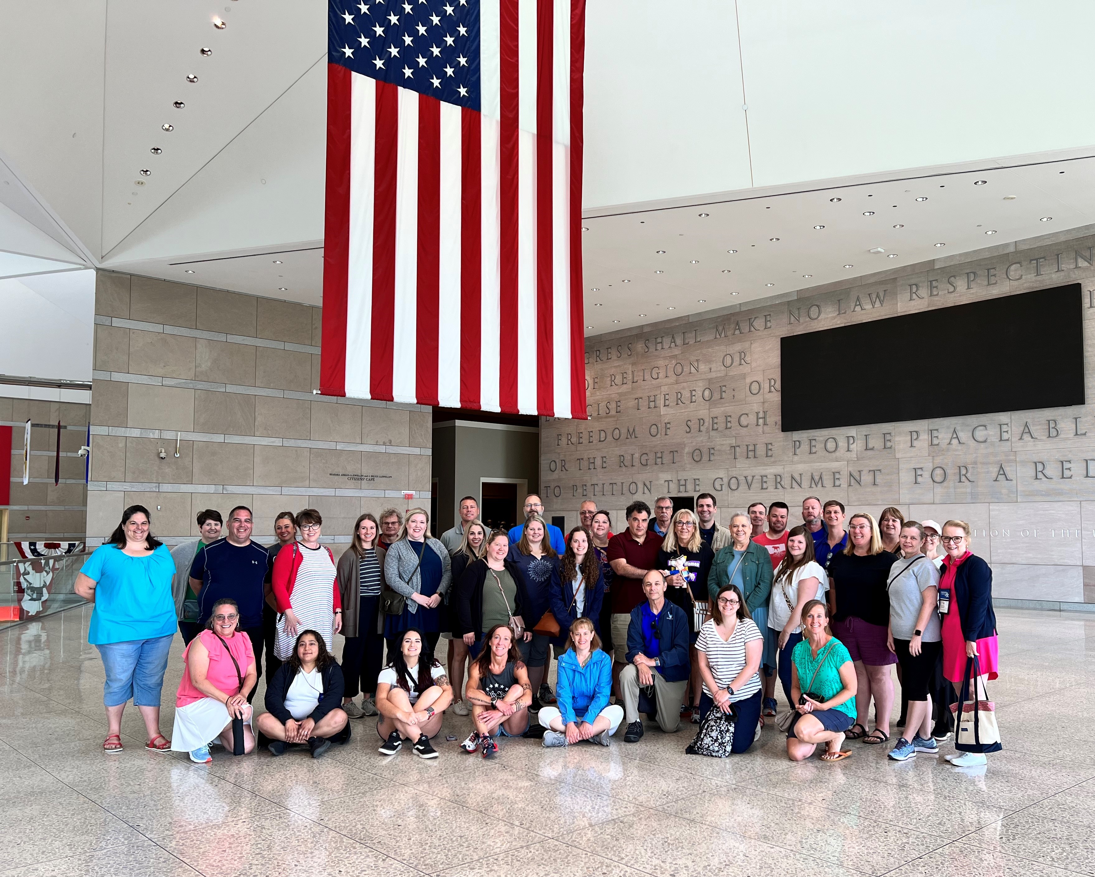 Group shot of adults posing under an American flag handing from a ceiling inside a building.