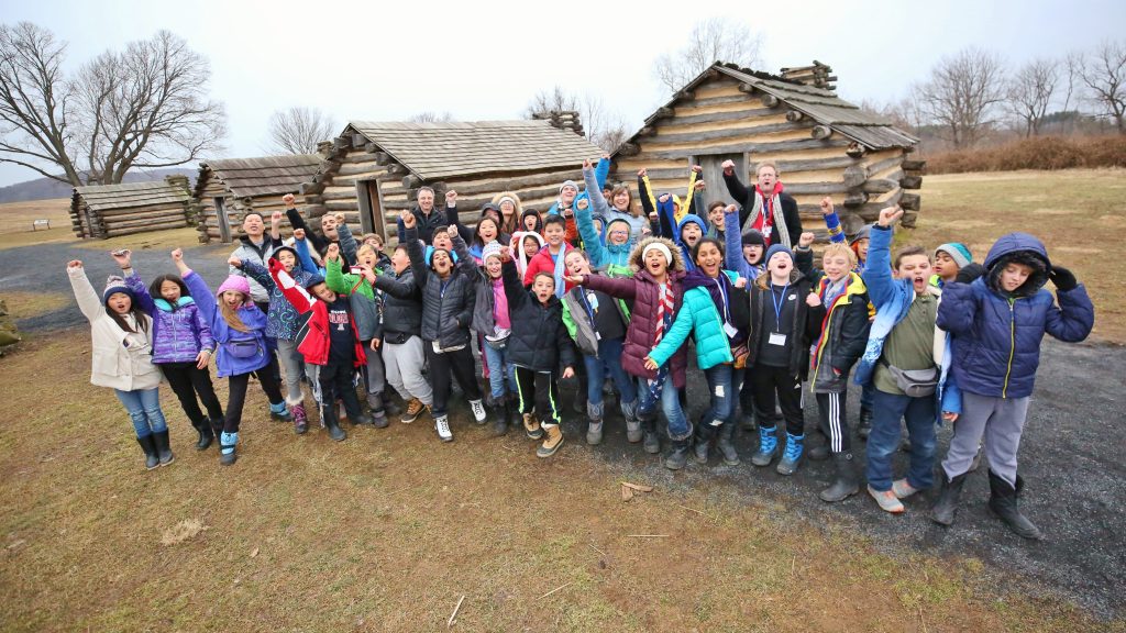 Students punching air in front of wooden cabins