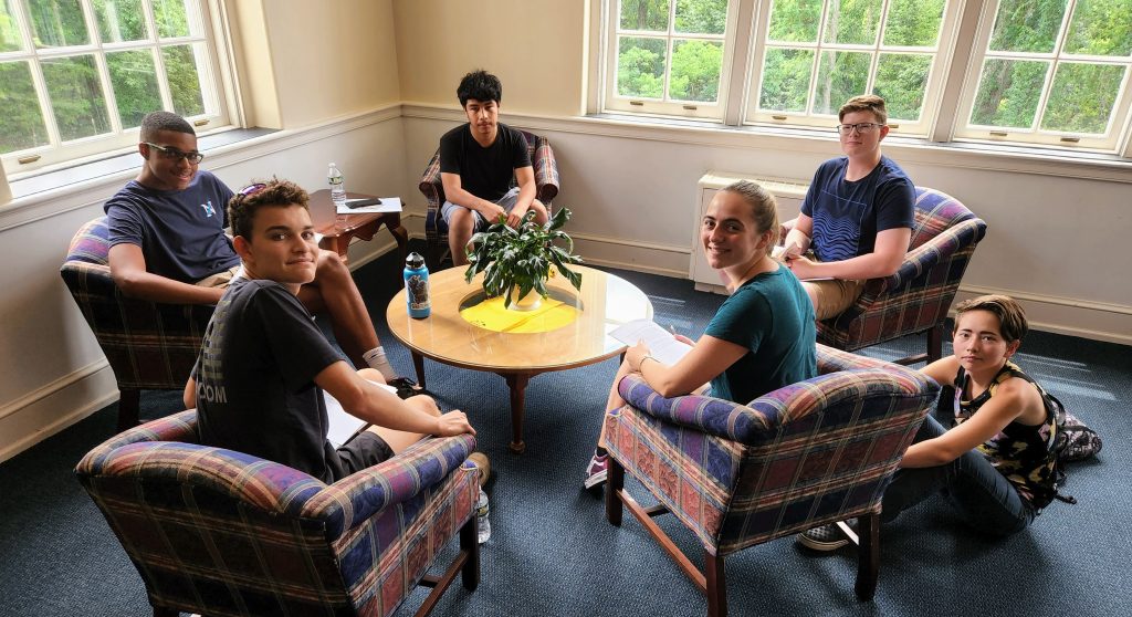 Students sitting around table in chairs and on floor